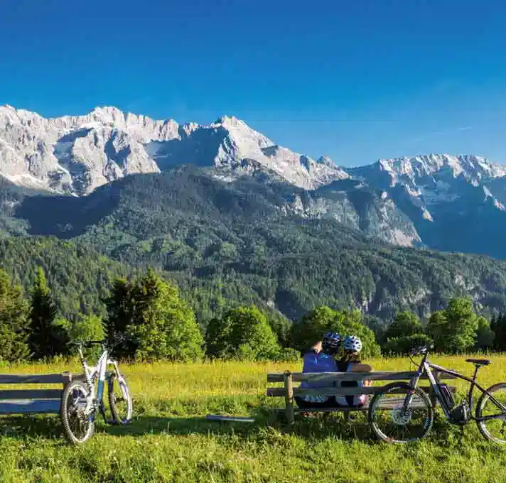 Zwei Radfahrer sitzen auf einer Bank und genießen das Alpenwelt Panorama